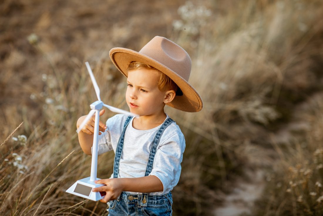Enfant avec un chapeau tenant une petite éolienne dans un champ
